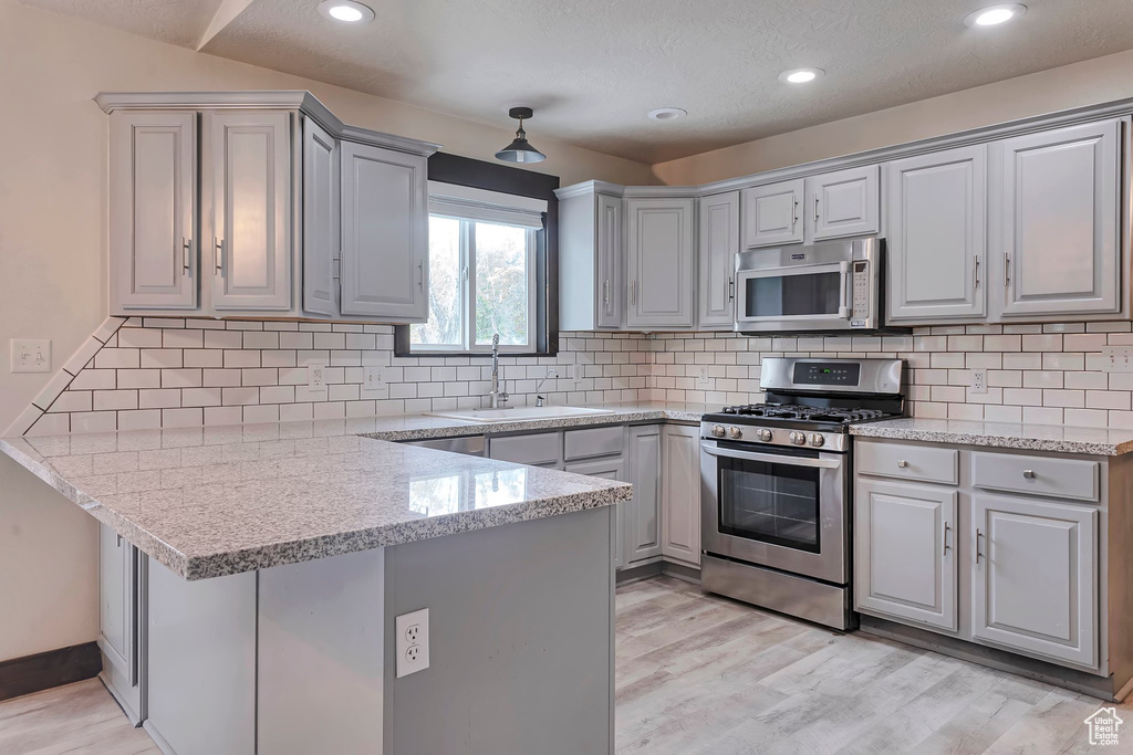 Kitchen with appliances with stainless steel finishes, a sink, a peninsula, gray cabinets, and light wood-style floors