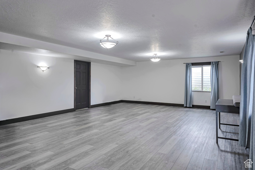 Below grade area featuring a textured ceiling, baseboards, and light wood-style floors