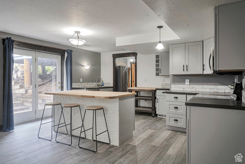 Kitchen with wood counters, stainless steel appliances, a textured ceiling, a breakfast bar, and light wood finished floors