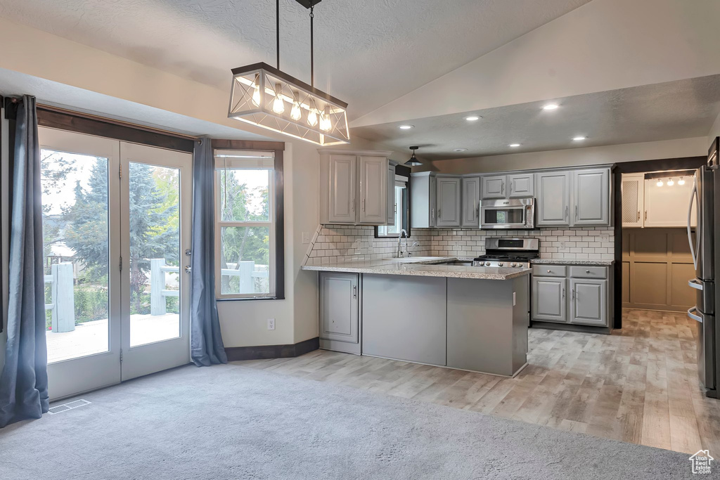 Kitchen featuring appliances with stainless steel finishes, gray cabinets, a peninsula, lofted ceiling, and tasteful backsplash