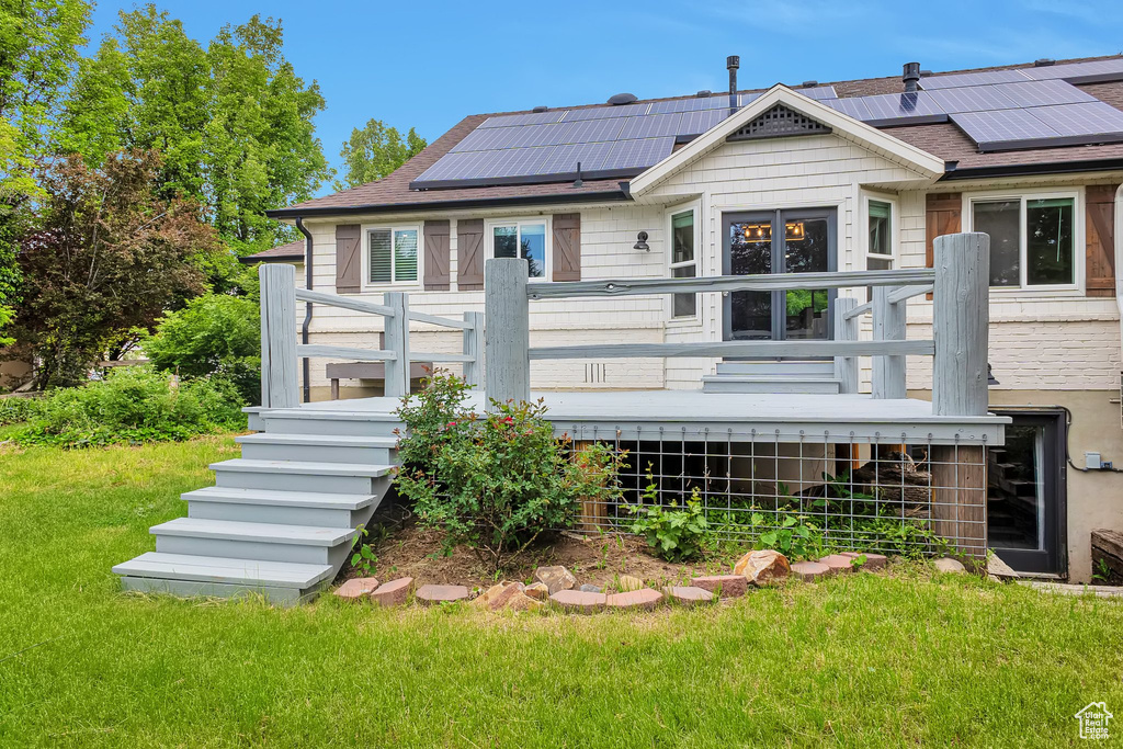 Back of property with a yard, roof mounted solar panels, and a wooden deck