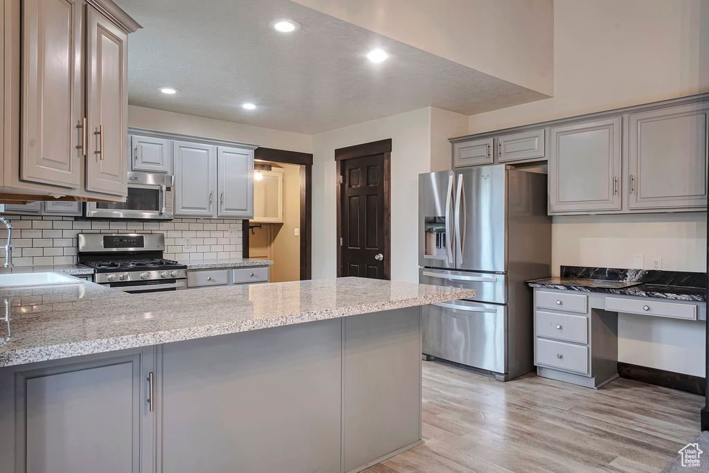 Kitchen with appliances with stainless steel finishes, gray cabinetry, a sink, a peninsula, and light wood-style floors