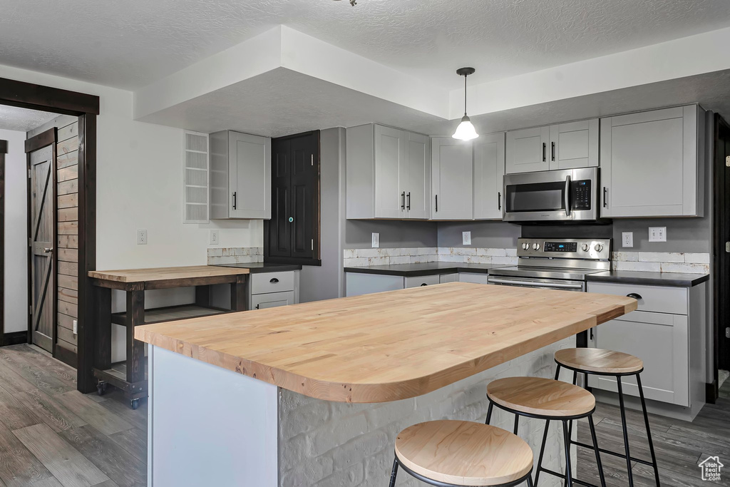 Kitchen featuring stainless steel appliances, wood counters, dark wood-style floors, a textured ceiling, and a kitchen breakfast bar