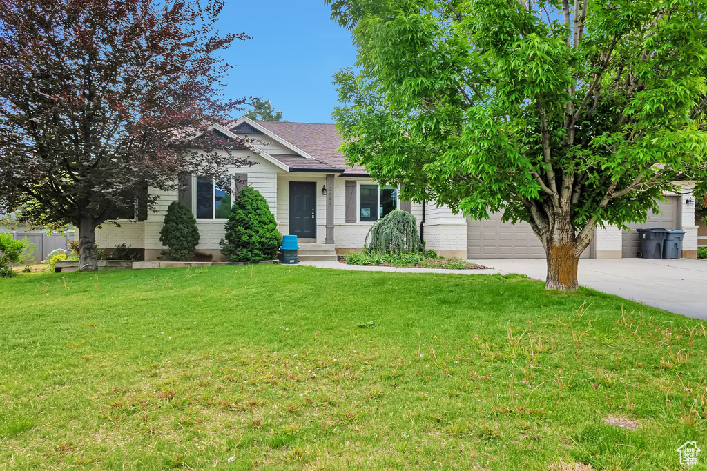View of front facade featuring concrete driveway, a front yard, and an attached garage