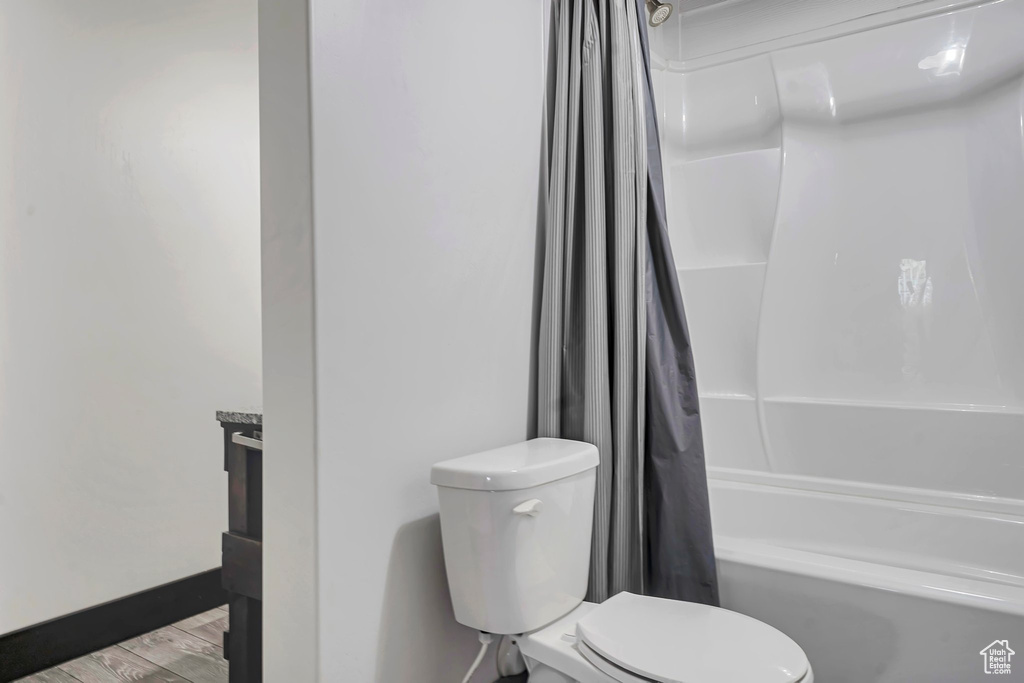Bathroom featuring toilet, wood finished floors, and shower / bathtub combination with curtain