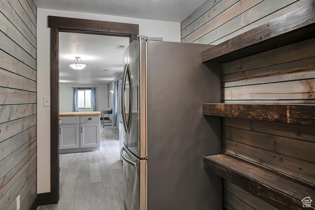 Kitchen featuring wood walls, light wood-style floors, butcher block counters, a textured ceiling, and freestanding refrigerator