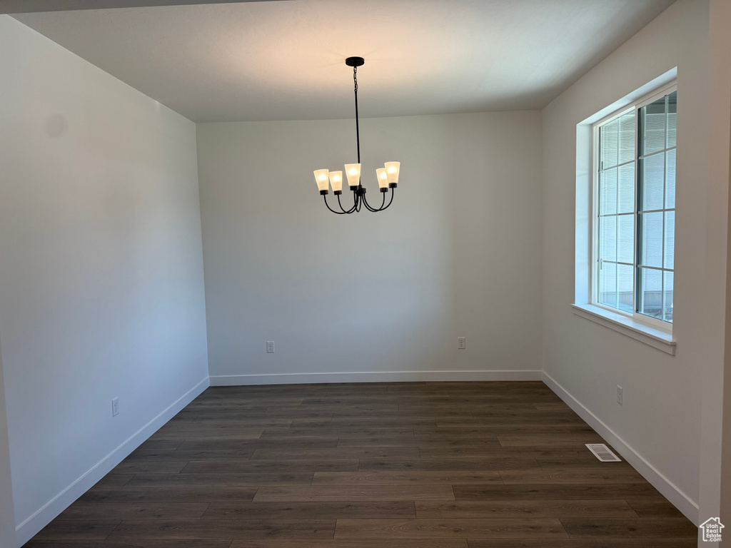 Unfurnished room featuring a chandelier, dark wood finished floors, and baseboards