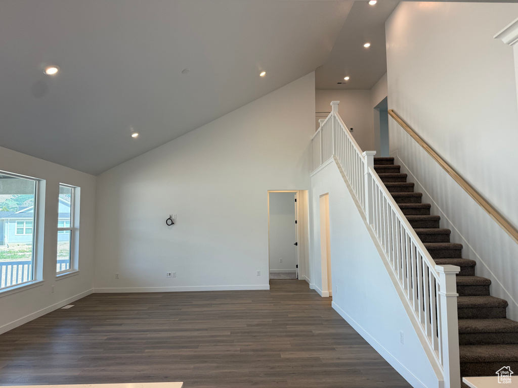 Unfurnished living room with high vaulted ceiling, stairs, baseboards, dark wood finished floors, and recessed lighting