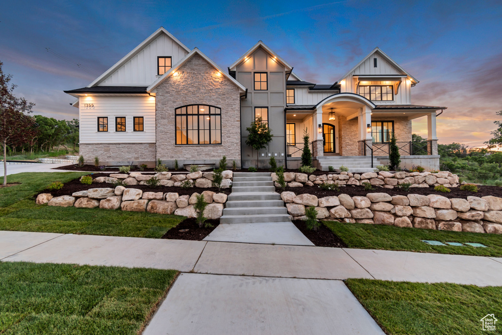 Modern farmhouse style home with board and batten siding, stone siding, a porch, a front lawn, and stairway