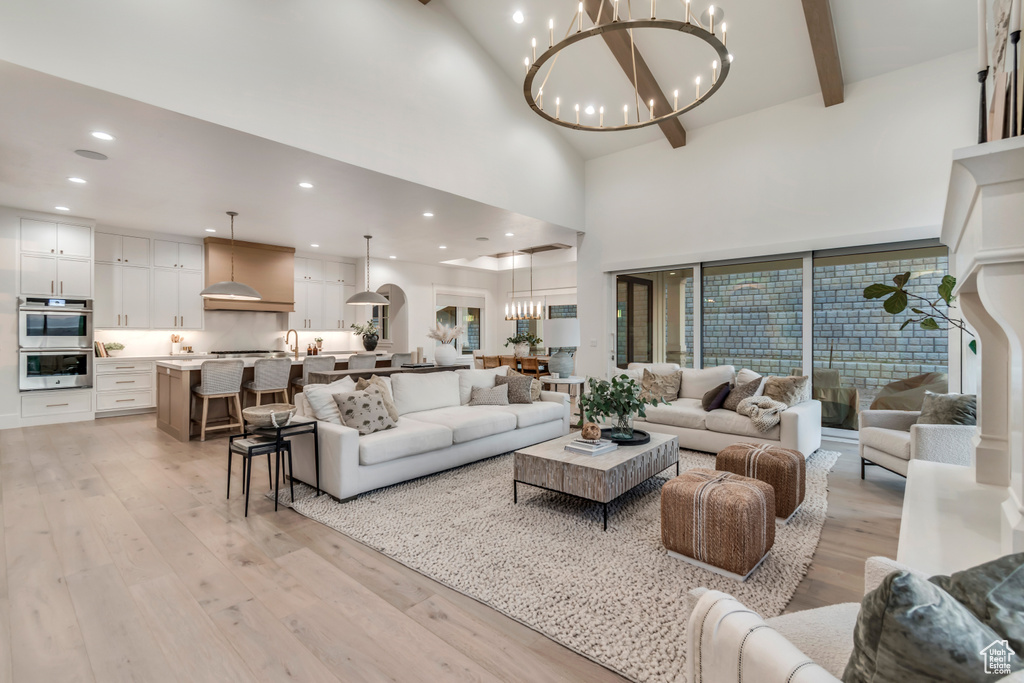 Living room with a chandelier, light wood finished floors, high vaulted ceiling, beamed ceiling, and recessed lighting