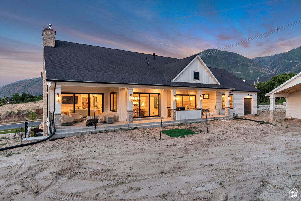 Back of house at dusk with a chimney, a mountain view, board and batten siding, and covered porch