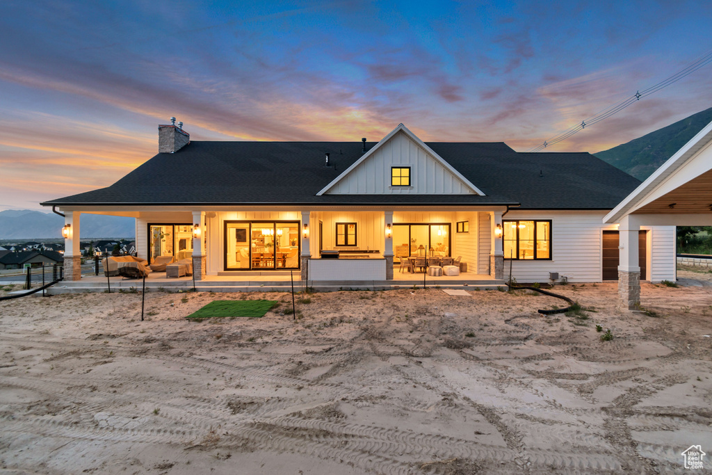 Back of property featuring board and batten siding, a chimney, a porch, and a shingled roof