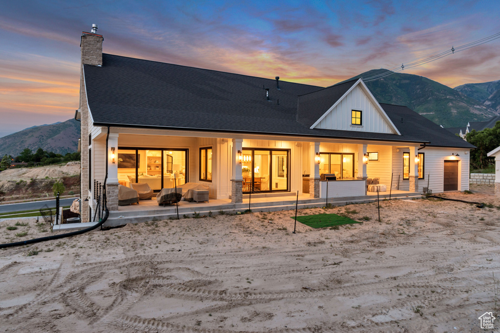 Back of property at dusk featuring a chimney, a mountain view, an attached garage, board and batten siding, and covered porch