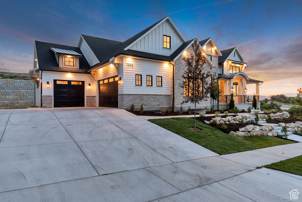 Modern farmhouse style home with board and batten siding, stone siding, concrete driveway, an attached garage, and a front lawn