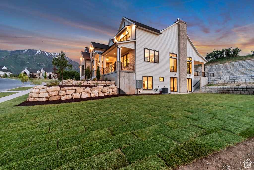 Rear view of property featuring a lawn, central air condition unit, a balcony, a chimney, and stairway