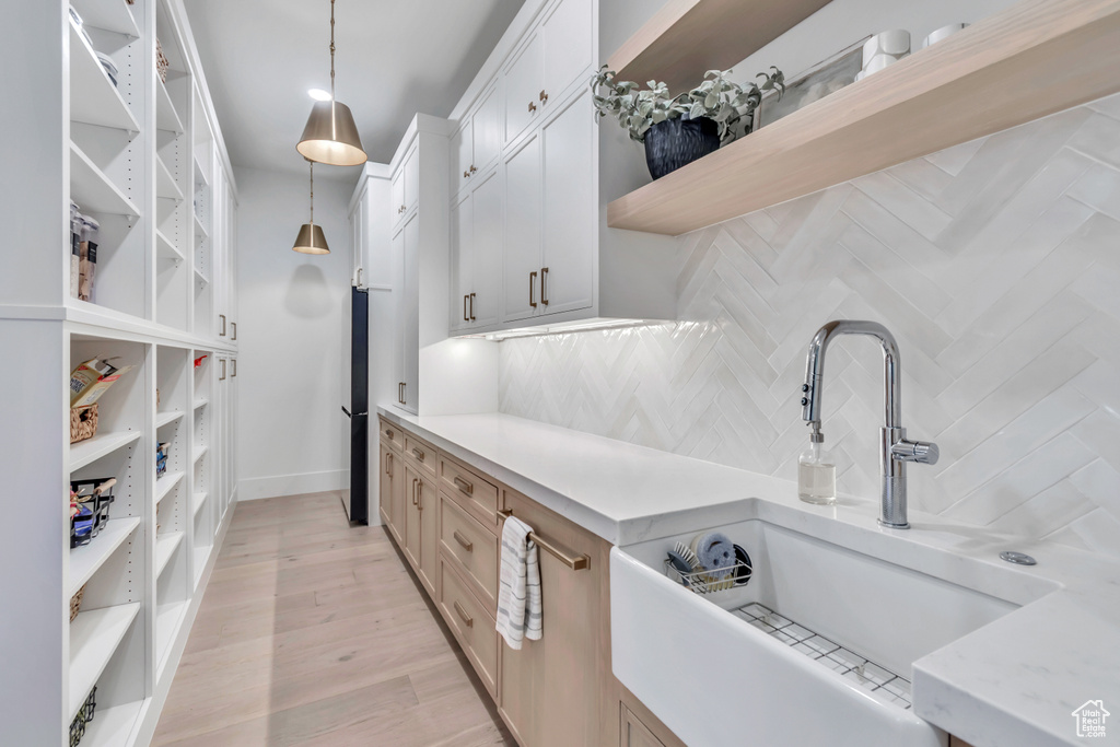 Kitchen featuring open shelves, a sink, decorative backsplash, hanging light fixtures, and white cabinetry