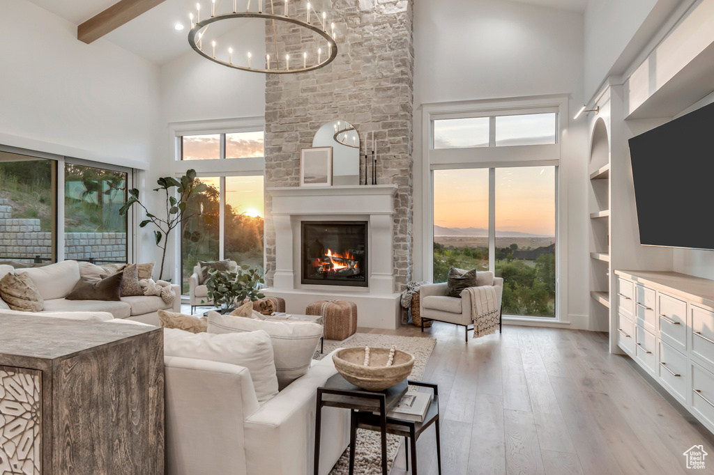 Living room featuring high vaulted ceiling, light wood-style flooring, a chandelier, a large fireplace, and beamed ceiling