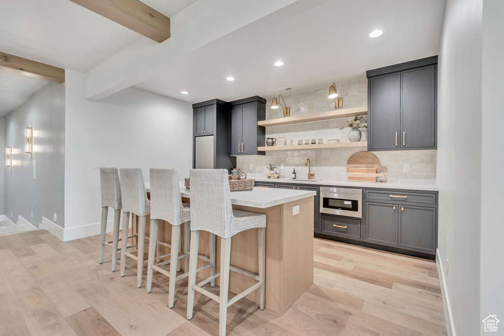Kitchen with oven, beamed ceiling, open shelves, tasteful backsplash, and light wood finished floors