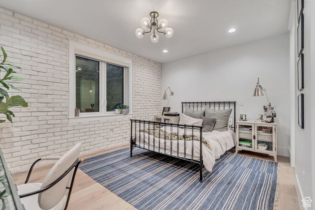 Bedroom with brick wall, wood finished floors, a chandelier, and recessed lighting