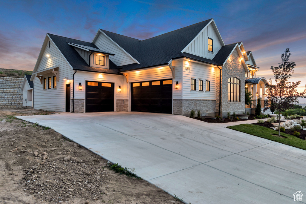 Modern farmhouse style home featuring stone siding, a garage, concrete driveway, and board and batten siding