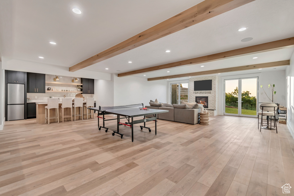 Recreation room featuring beamed ceiling, light wood-type flooring, bar with sink, recessed lighting, and a fireplace