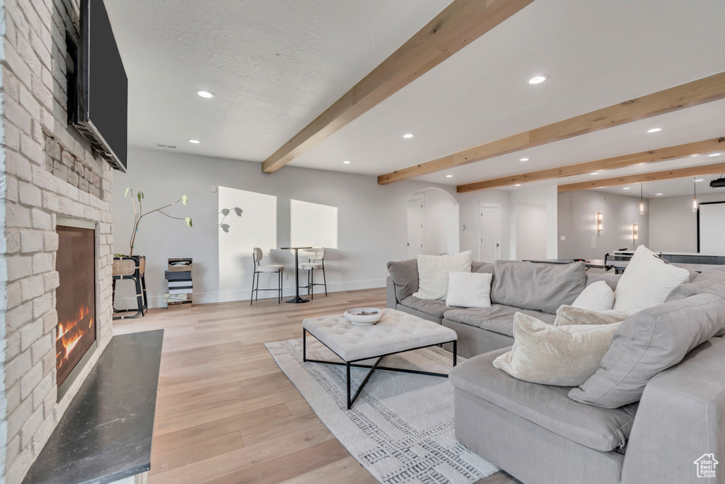 Living area with a fireplace, beam ceiling, recessed lighting, light wood-style floors, and baseboards