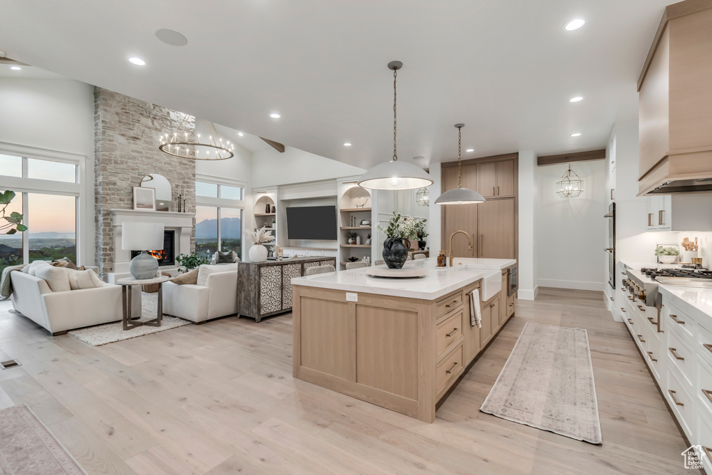 Kitchen featuring a sink, stainless steel gas stovetop, light countertops, high vaulted ceiling, and an island with sink