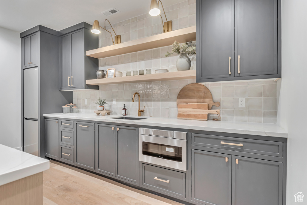 Kitchen featuring gray cabinetry, open shelves, a sink, and decorative backsplash