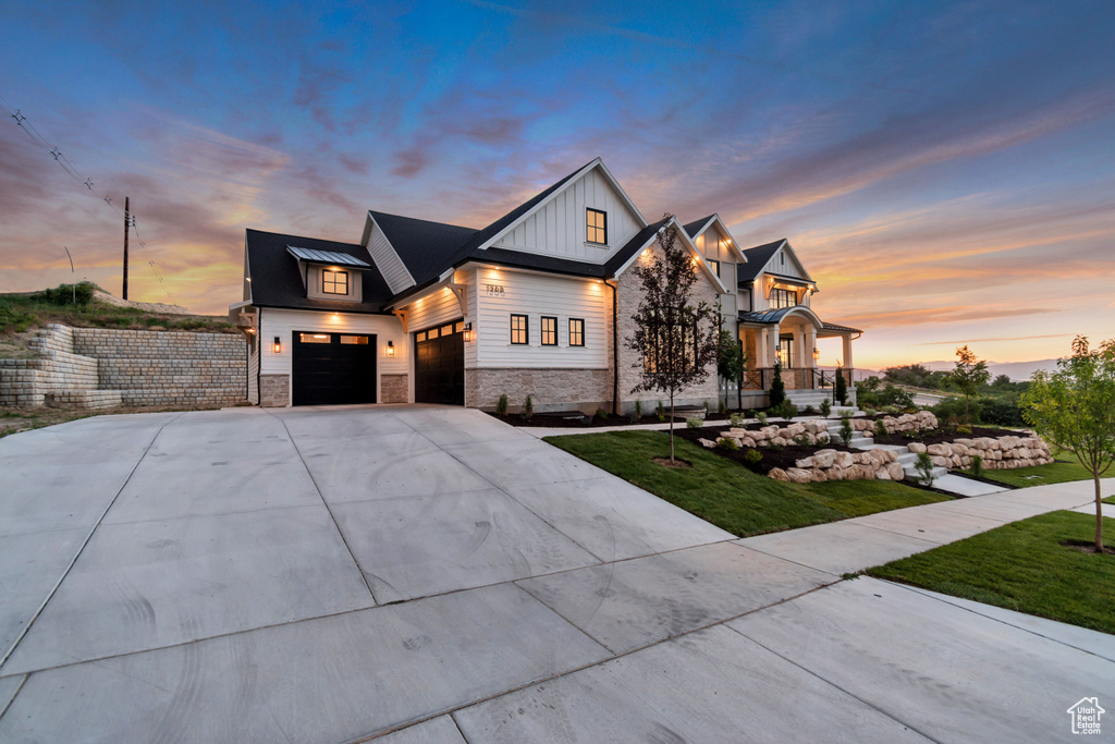 View of front of home with stone siding, board and batten siding, a standing seam roof, concrete driveway, and a lawn