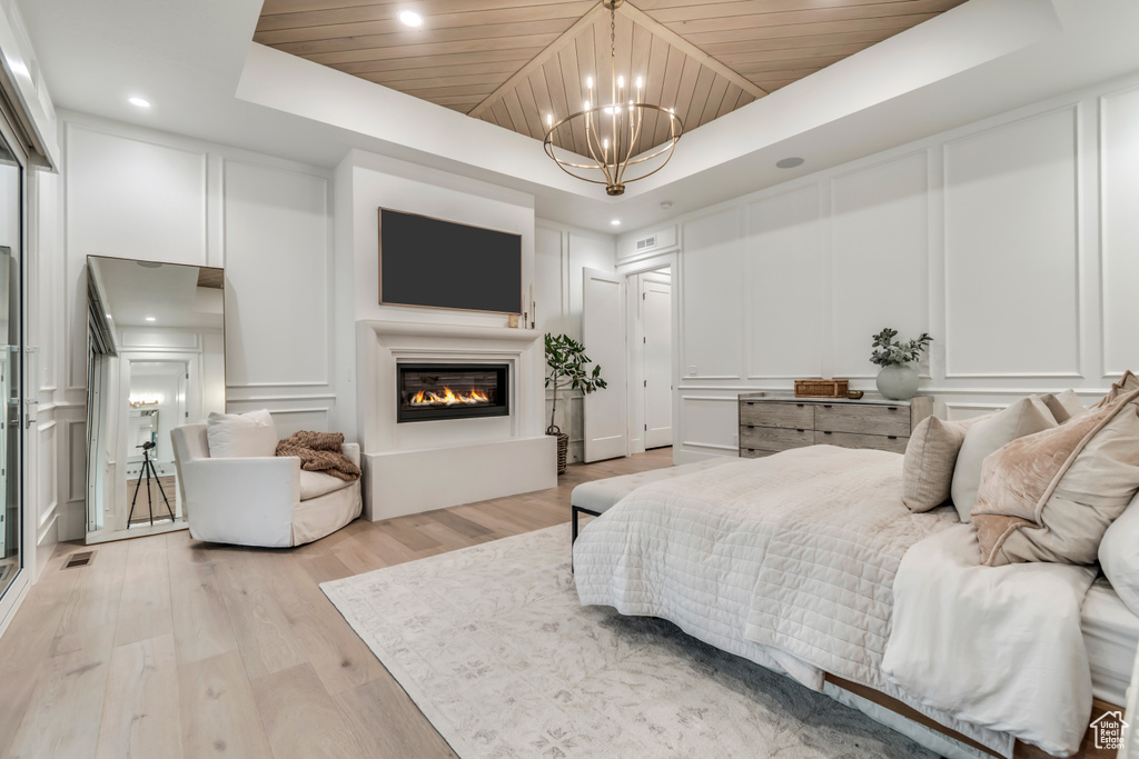 Bedroom with a decorative wall, a raised ceiling, a chandelier, light wood-style flooring, and wooden ceiling