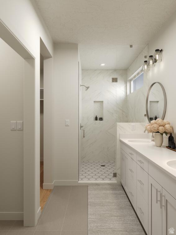 Full bathroom featuring a marble finish shower, double vanity, tile patterned flooring, baseboards, and a textured ceiling