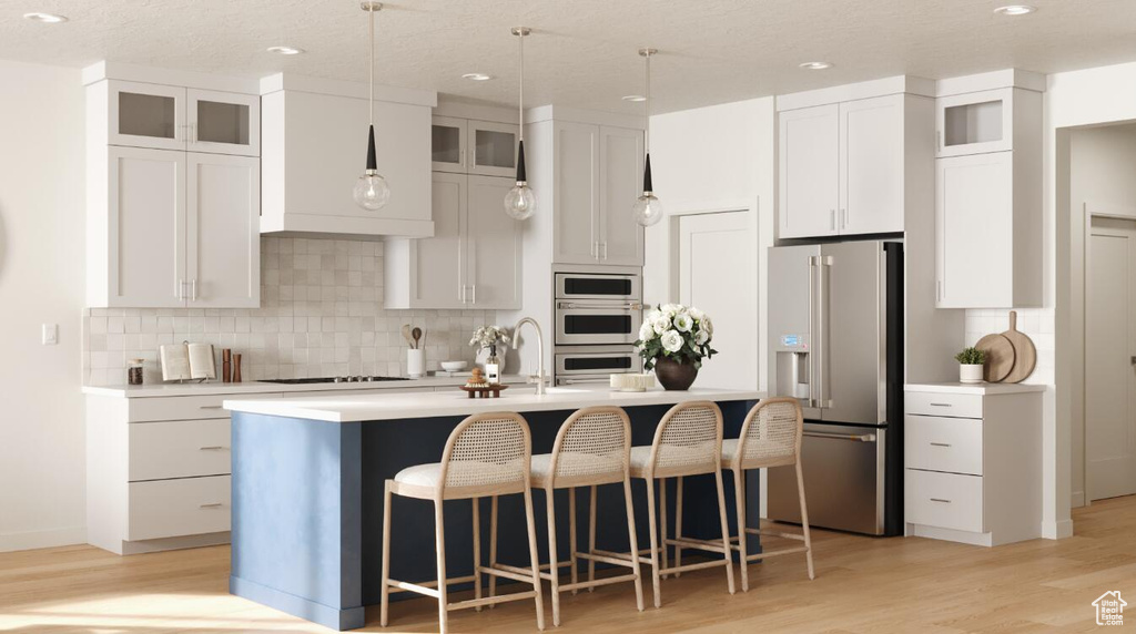 Kitchen featuring high end fridge, an island with sink, light countertops, backsplash, and recessed lighting