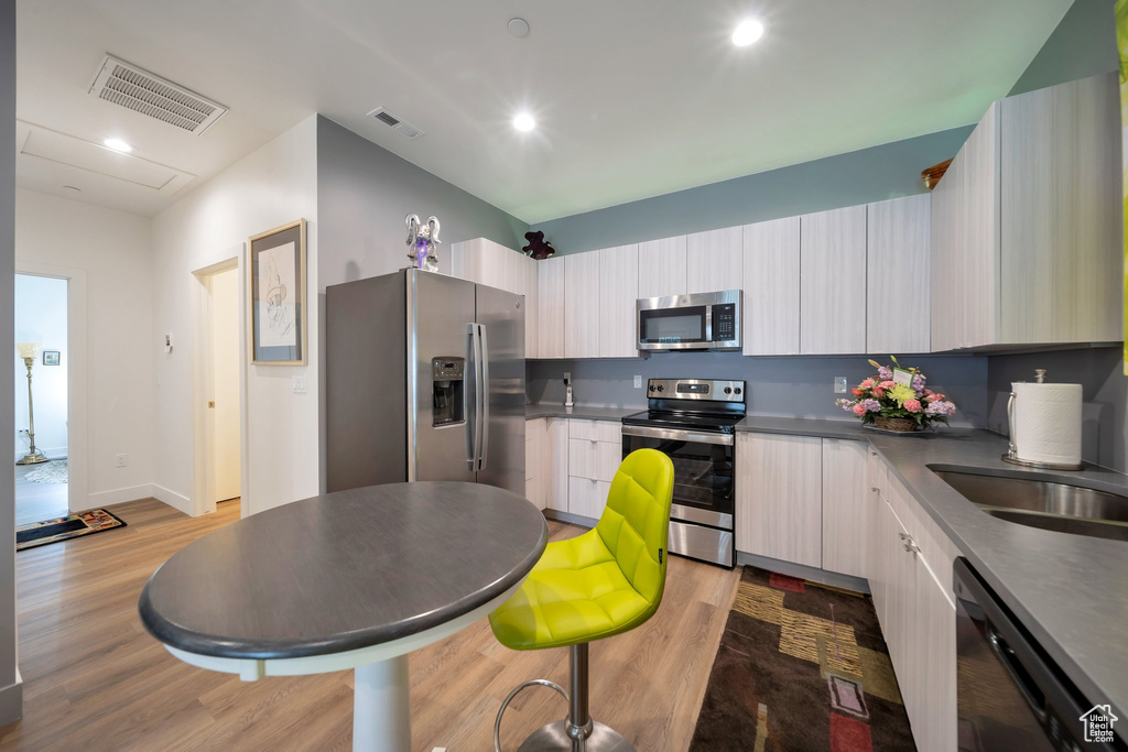 Kitchen with appliances with stainless steel finishes, light wood finished floors, modern cabinets, dark countertops, and recessed lighting
