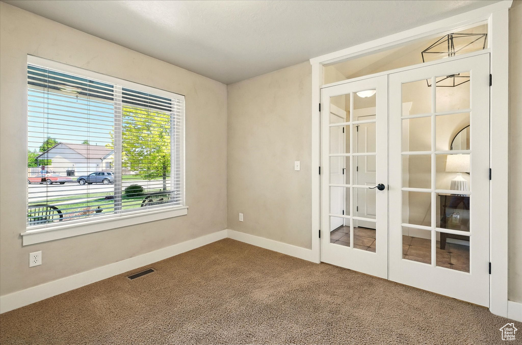 Carpeted empty room featuring french doors and baseboards