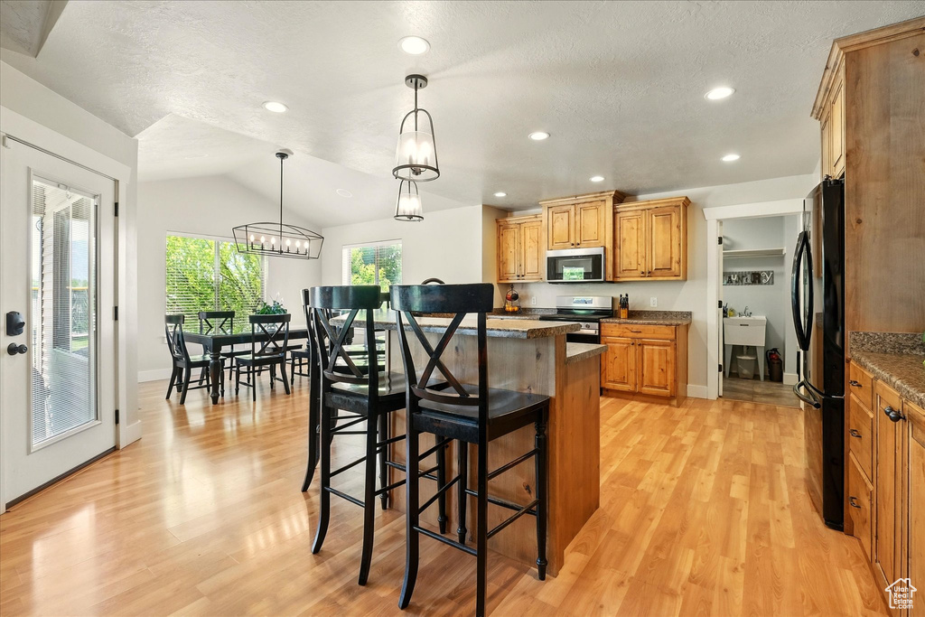 Kitchen featuring appliances with stainless steel finishes, a kitchen bar, light wood finished floors, a center island, and recessed lighting
