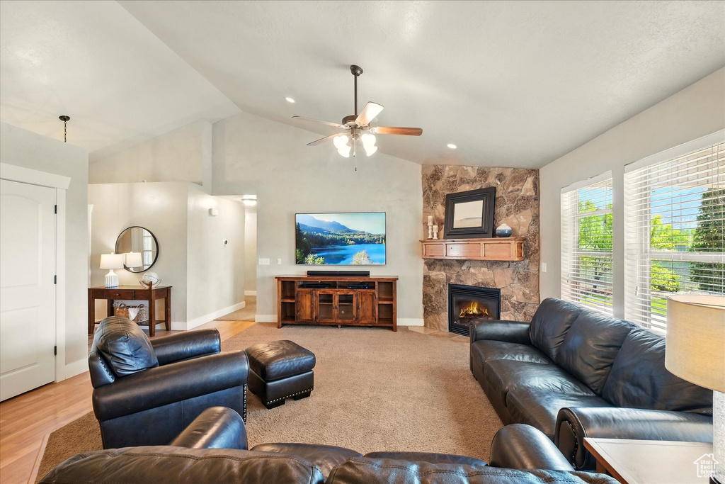 Living room with a ceiling fan, a stone fireplace, baseboards, and high vaulted ceiling