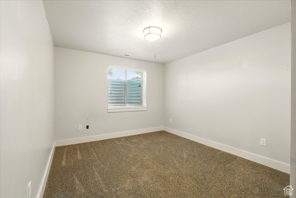 Empty room with dark carpet, baseboards, and a textured ceiling