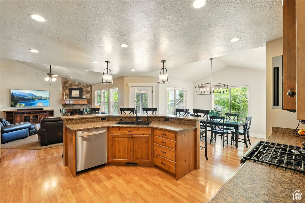 Kitchen with vaulted ceiling, a sink, dishwasher, a breakfast bar, and light wood-type flooring