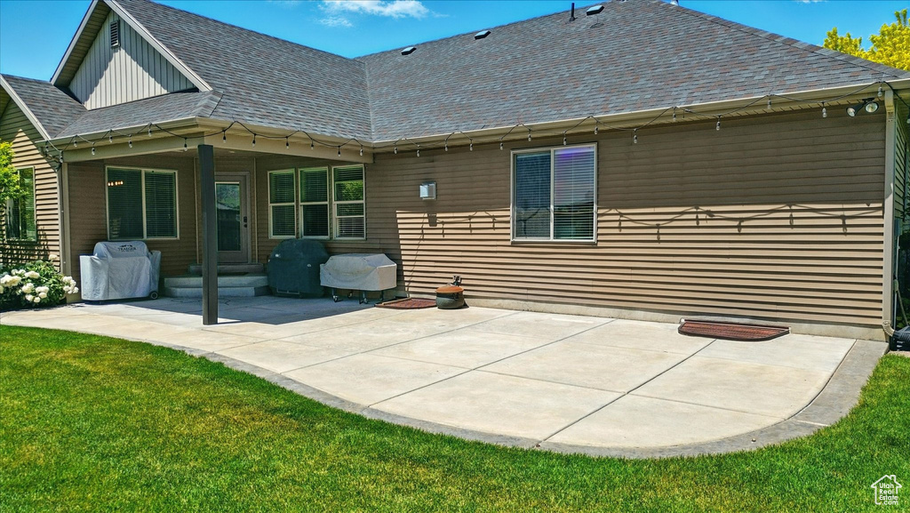 Rear view of house with a patio area, a lawn, and a shingled roof