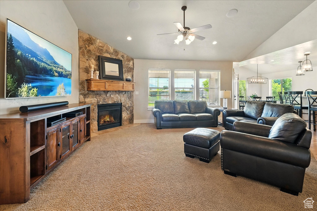 Living area featuring vaulted ceiling, light colored carpet, a ceiling fan, a fireplace, and a chandelier
