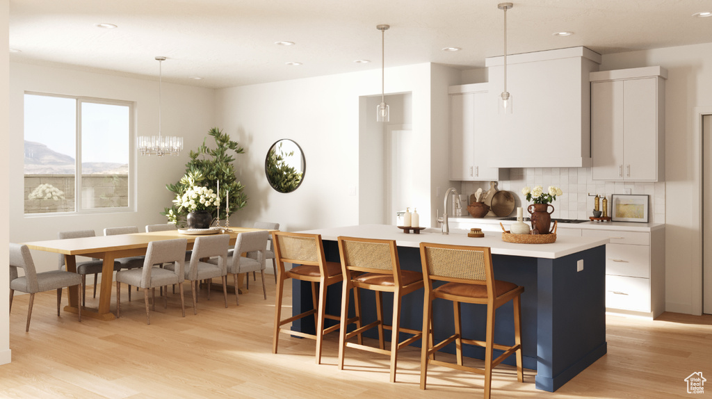 Kitchen with a kitchen island with sink, a breakfast bar, light wood finished floors, light countertops, and tasteful backsplash