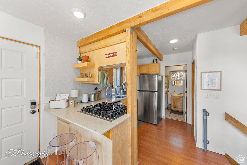 Kitchen featuring stainless steel appliances, a sink, light countertops, light brown cabinetry, and light wood-style floors