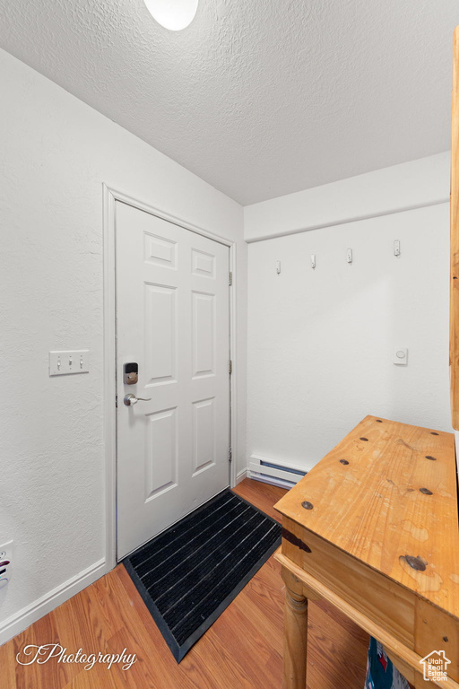 Entrance foyer featuring wood finished floors, baseboards, a baseboard radiator, and a textured ceiling