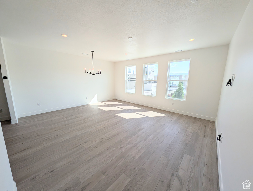 Unfurnished room with a chandelier, light wood-style floors, baseboards, and recessed lighting
