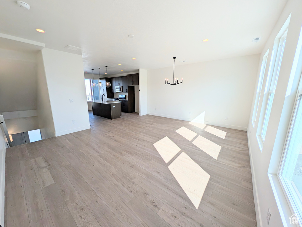 Unfurnished living room featuring a chandelier, a sink, light wood finished floors, recessed lighting, and baseboards