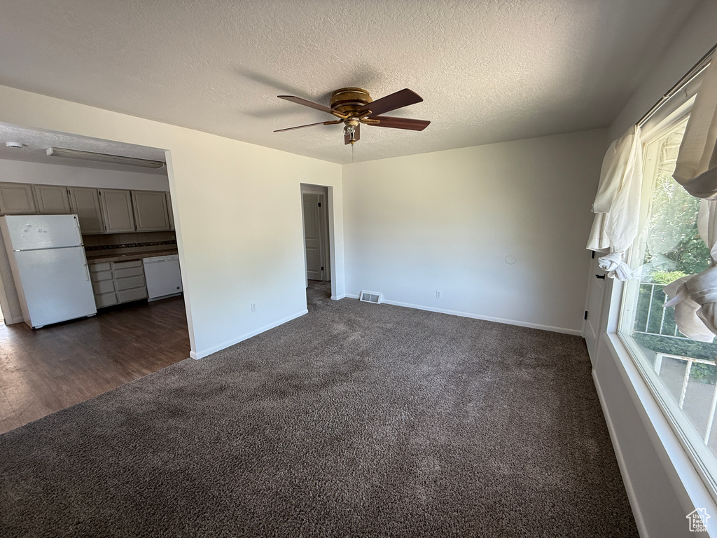 Unfurnished living room with dark carpet, a ceiling fan, baseboards, and a textured ceiling