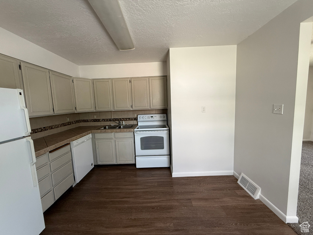 Kitchen featuring white appliances, tile counters, dark wood-type flooring, a textured ceiling, and a sink