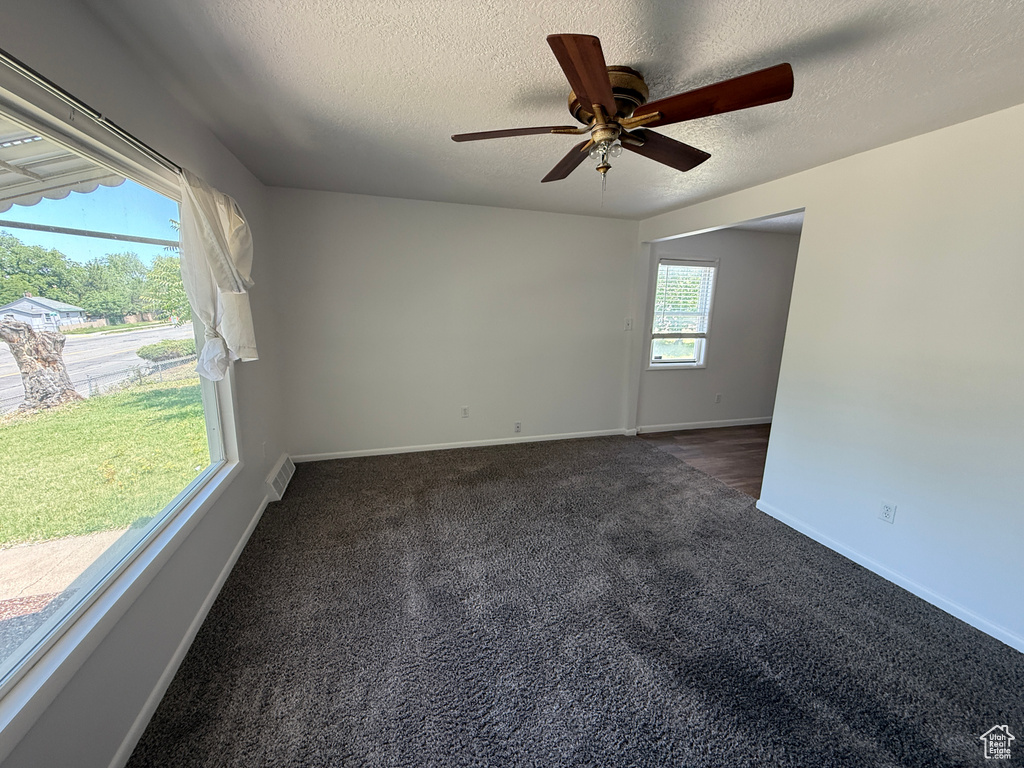 Empty room featuring dark colored carpet, a textured ceiling, ceiling fan, and baseboards