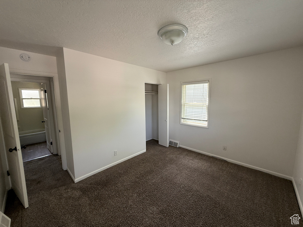 Unfurnished bedroom with multiple windows, dark carpet, baseboards, and a textured ceiling