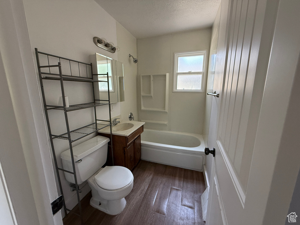 Bathroom with toilet, vanity, wood finished floors, shower / washtub combination, and a textured ceiling